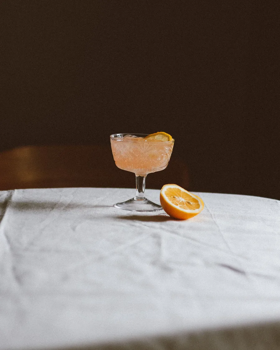 A citrus mocktail in a coupe glass beside a lemon half, in dramatic low light