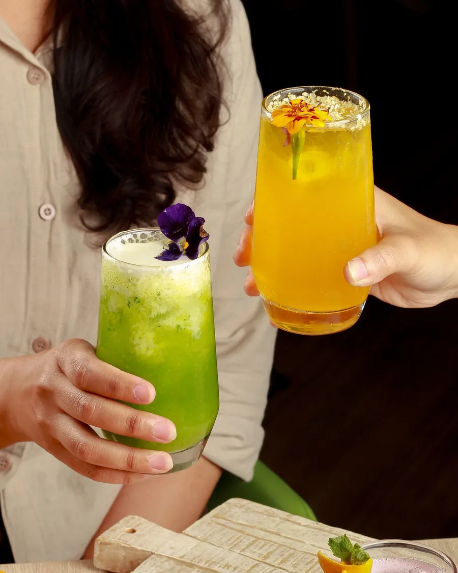 Two people toasting colorful non-alcoholic drinks garnished with edible flowers
