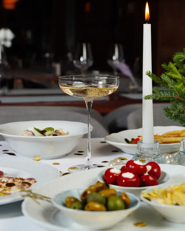 A candlelit holiday table with a coupe of sparkling wine