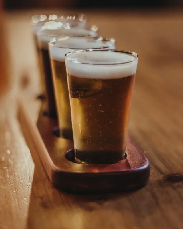 A flight of amber beers on a wooden paddle