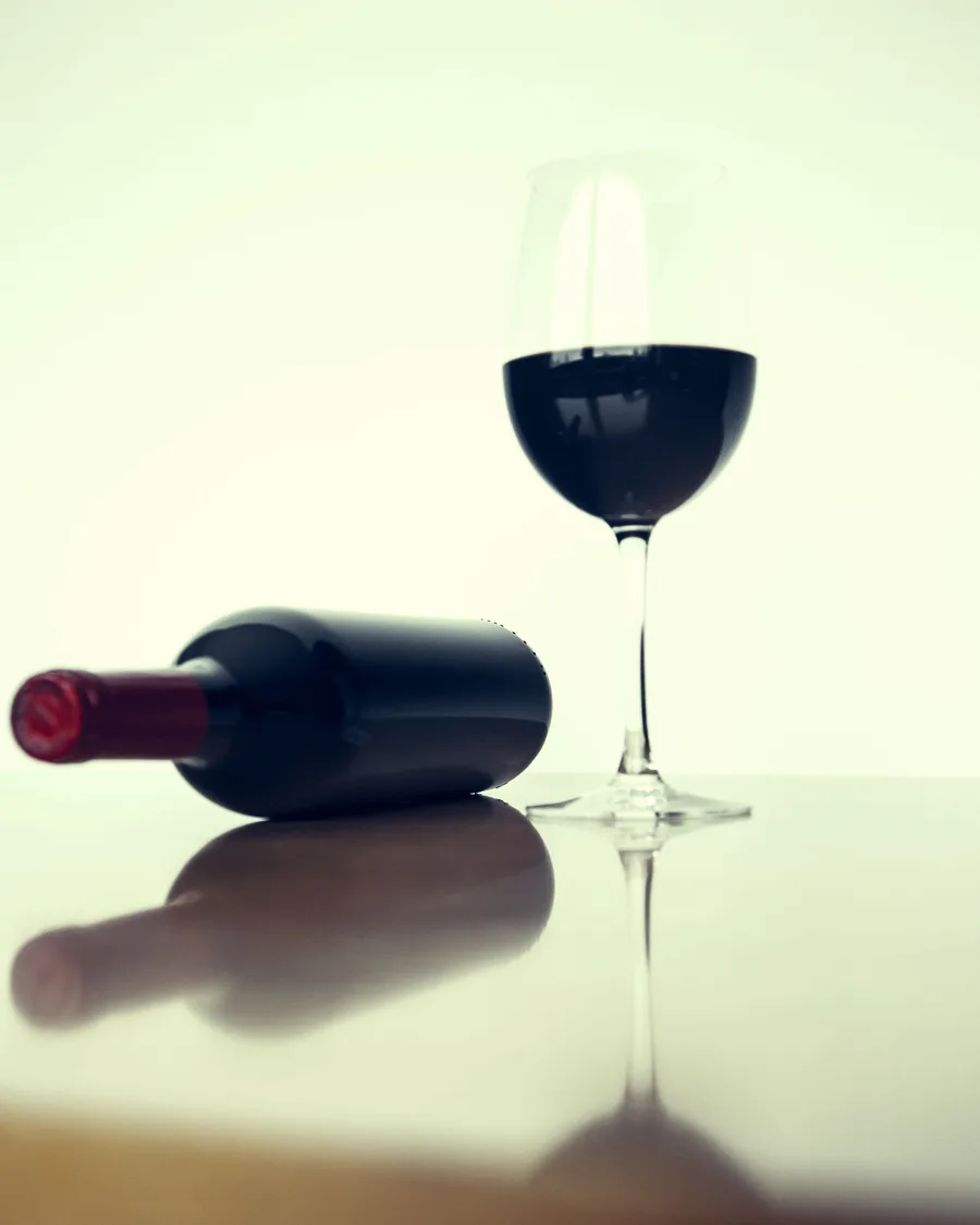 A glass of red wine and a reclining wine bottle on a reflective surface